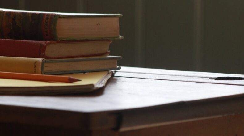 Close-up of stacked books and a pencil on a wooden table, suggesting a study environment.
