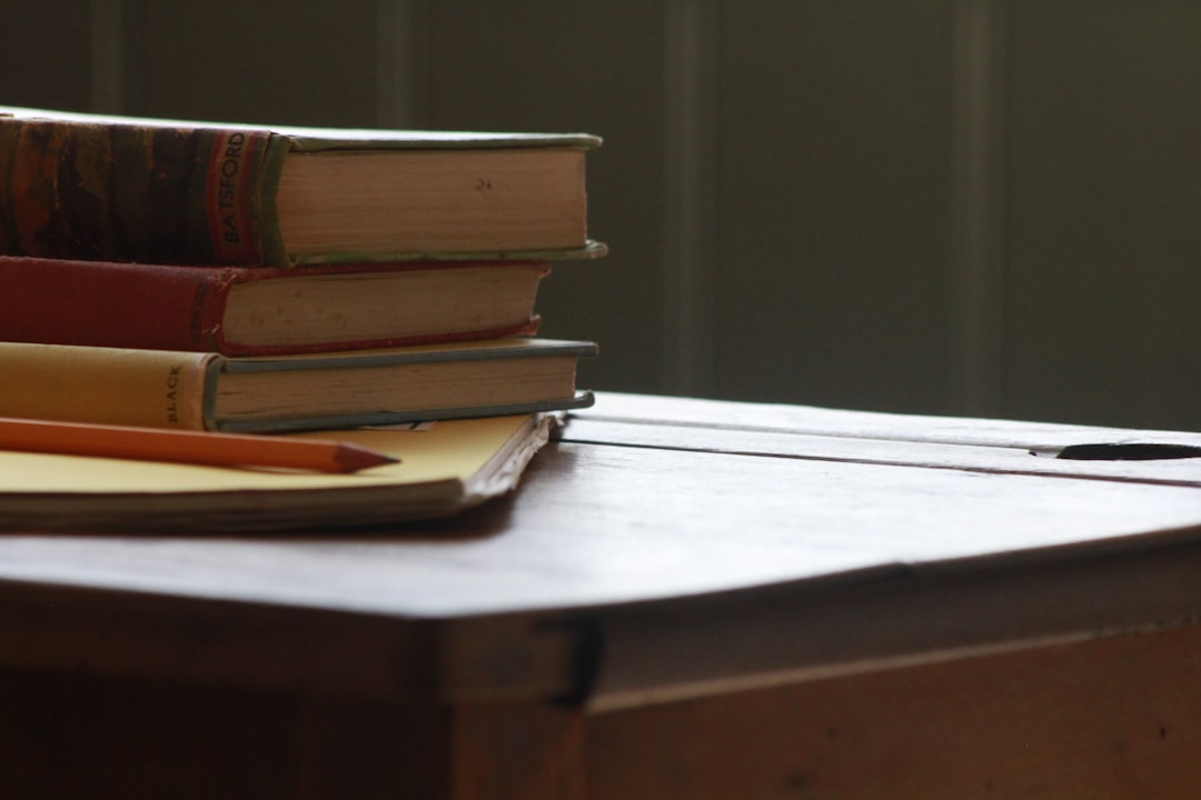 Close-up of stacked books and a pencil on a wooden table, suggesting a study environment.