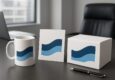 A white coffee mug, a greeting card, and a box with blue wave designs on a table in an office setting.