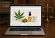 A laptop displaying cannabis products, including a leaf, oil, and a container, on a desk with scales in the background.